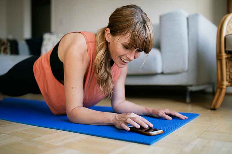 photo of a woman exercising at home with a virtual trainer on her phone